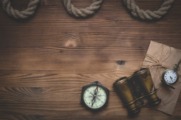 Travel or adventure flat lay background with a copy space. Binoculars, pocket watch, old parchment, mooring rope and a compass on a wooden table.