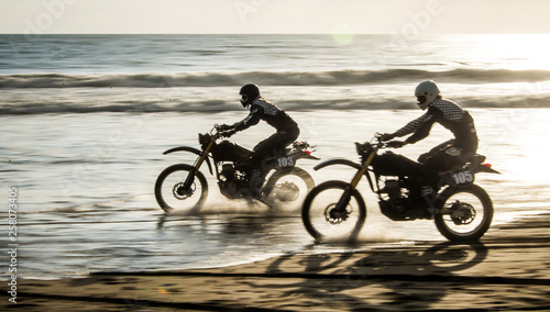 Fotomural Two friends racing on custom retro style cafe racer black motorcycles on the bea
