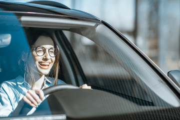 Wall Mural - Young and happy woman driving a luxury car, front view through the windshield with sunlight