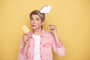 Waist up of thoughtful woman holding white paper cloud and gold card