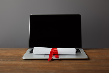 Wall Mural - Laptop with blank screen and diploma with red ribbon on wooden surface on grey