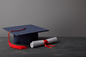 Poster - Diploma and academic cap with red tassel on dark surface on grey