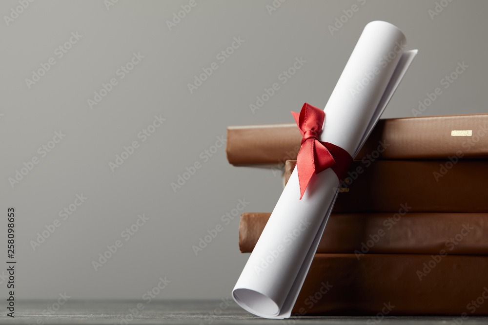 Brown books and diploma with red ribbon isolated on grey - obrazy, fototapety, plakaty 