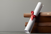 Brown Books And Diploma With Red Ribbon Isolated On Grey