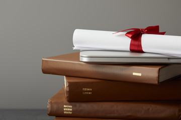 Wall Mural - Brown books, laptop and diploma with red ribbon isolated on grey