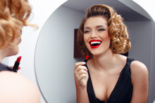 Elegant, smiling young woman, model with charming hairstyle and evening make up, applying red lipstick on sensual lips.