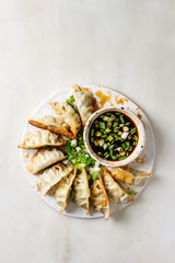 Fried asian dumplings Gyozas potstickers in white ceramic plate served with bowl of soy onion sauce over white marble background. Flat lay, space