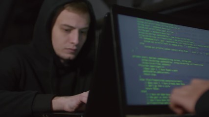 Wall Mural - rack focused shot of two programmers sitting at table in darkness and typing parts of program code