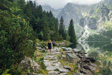 back view of young women in sportswear hiking on the stony pathway, and cliffs in mountains. morskie