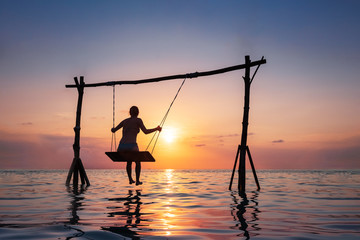 Happy girl relaxing at the beach on rope swing above sea water at sunset, summer vacation holidays resort