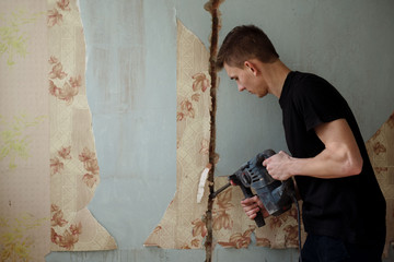 A young man drills a wall with a perforator