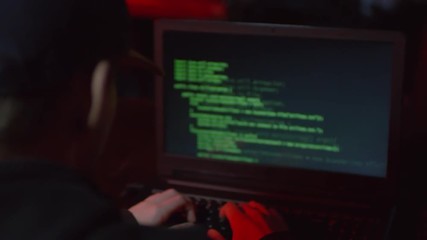 Wall Mural - back view of hacker sitting at laptop, typing on keyboard and breaking into system