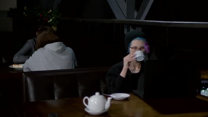 Wall Mural - sequence of videos with young caucasian woman in hoodie and hat sitting at café table at laptop, typ