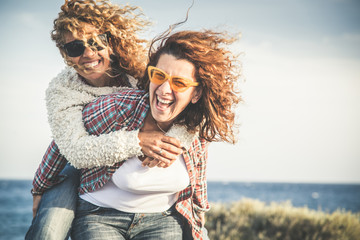 Portrait of two pretty woman enjoy free time. Smiling middle age girls giving her laughing friend piggyback while enjoying the day together at the beach. Best friends smiling and playing together