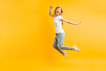 Portrait of a cheerful enthusiastic girl in a white T-shirt jumping for joy on a yellow background