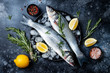 © sveta_zarzamora - Fresh raw seabass fish on black stone background with spices, herbs, lemon and salt. Culinary seafood background with ingredients for cooking. Top view