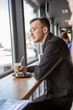 © Максим Галінский - Young stylish man enjoys a cake and a drink while sitting in a cafe with large windows