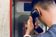Back View Of Young Man Making A Call From Public Phone Box