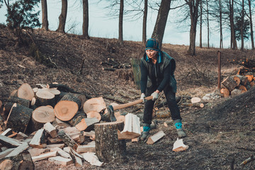 A rural woman shoots an ash tree wood for harvesting for the winter with an ax