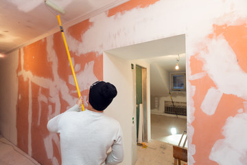 Wall Mural - Worker is painting the ceiling by paint roller in corridor an apartment is inder construction, remodeling, renovation, overhaul, extension, restoration and reconstruction. Concept of home improvement