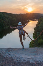 Girl Jumping From The Bridge. A Girl With An Incredible Time Is Engaged In Freestyle In Bungee Jumping. A Young Girl Performs A Reverse Trick In Bungee Jumping. Jump At Sunset Extreme Young.