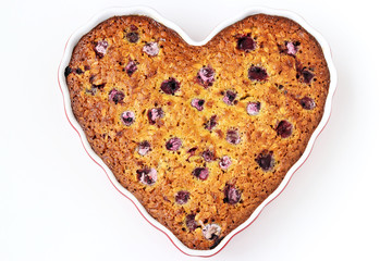 Oatmeal pie with cherry in the ceramic form in the shape of a heart on a white background