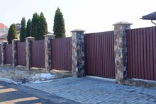 Part Of A Brown Fence With A Gate Made Of Wooden Planks And Stones Outside