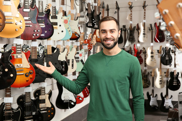 Wall Mural - Young shop assistant near guitars in music store