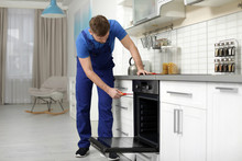 Professional Serviceman Repairing Modern Oven In Kitchen
