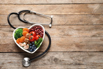 Bowl with heart-healthy diet products and stethoscope on wooden background, top view. Space for text