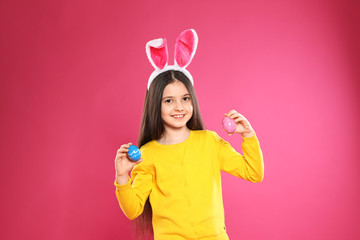 Sticker - Little girl in bunny ears headband holding Easter eggs on color background