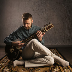 Portrait of a European man playing the sitar sitting on the carpet