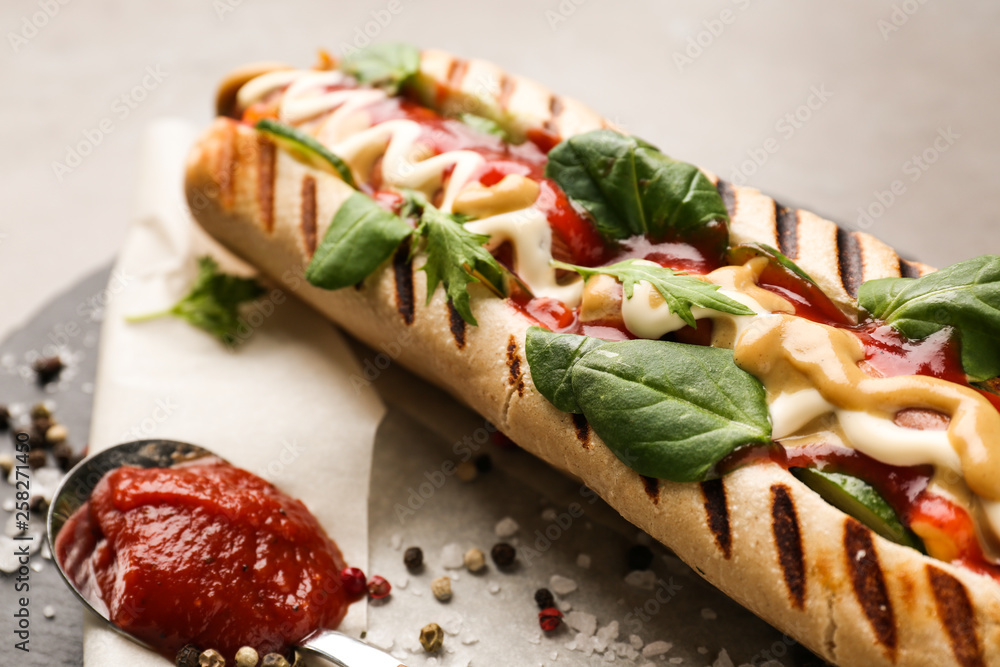 Tasty hot dog with sauce on slate plate, closeup