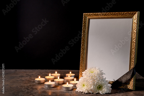 Blank Funeral Frame Candles And Flowers On Table Against Black