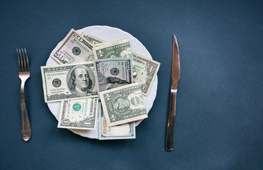 Money lying on the plate with fork and knife. Dollars photo. Greedy corruption concept. Bribe idea.