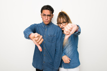 Wall Mural - Young couple with glasses showing thumb down sign with negative expression