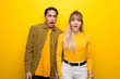 Young couple over vibrant yellow background with surprise and shocked facial expression