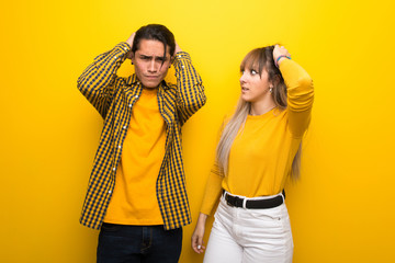 Wall Mural - Young couple over vibrant yellow background takes hands on head because has migraine