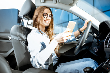 Young and cheerful woman using smart phone while driving a modern car in the city