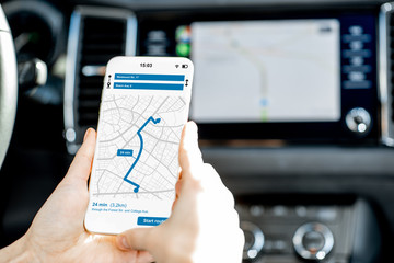 Close-up of a smartphone with navigation app in the modern car with monitor on the background