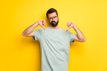 Wall Mural - Man with beard and green shirt showing thumb down with both hands