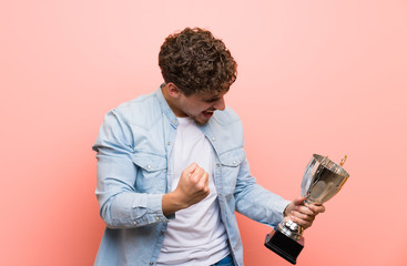 Wall Mural - Blonde man over pink wall holding a trophy