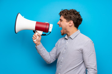 Wall Mural - Blonde man over blue wall shouting through a megaphone