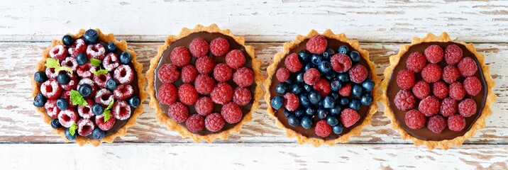 Raspberry and blueberry tartlets with chocolate ganache, fresh berries and mint leaves, selective focus. Fresh fruit tart on white background, freshly homemade fruit cake on a table