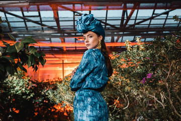 Gorgeous young woman in blue dress in turban in orangery