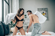 © LIGHTFIELD STUDIOS - cheerful brunette woman in lace underwear having pillow fight with muscular boyfriend on bed
