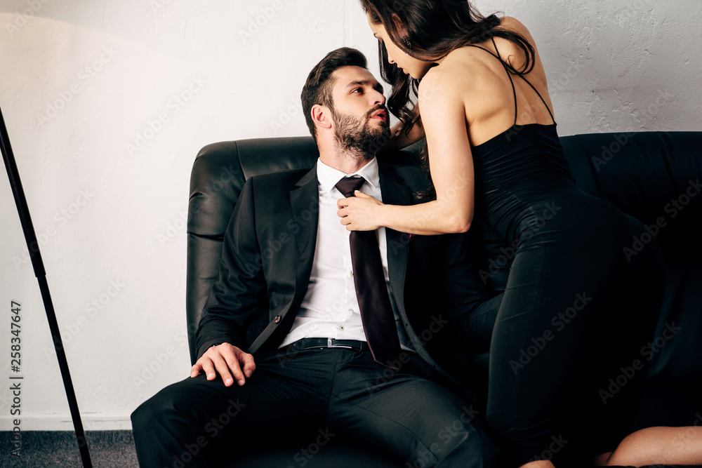 brunette girl in black dress holding tie of passionate man in suit ...
