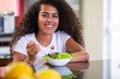 © paulovilela - cheerful young afro american woman eating vegetable salad in home kitchen.