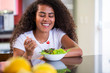 © paulovilela - cheerful young afro american woman eating vegetable salad in home kitchen.