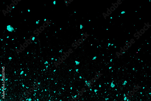 A splatter of green blue colored pigment powder on black background.